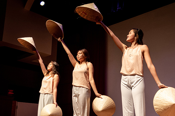 Three performers holding up straw hats.