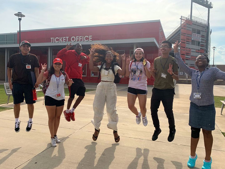 Group of people getting ready to pose for a picture together, person in front is holding a cellphone in order to take the picture.