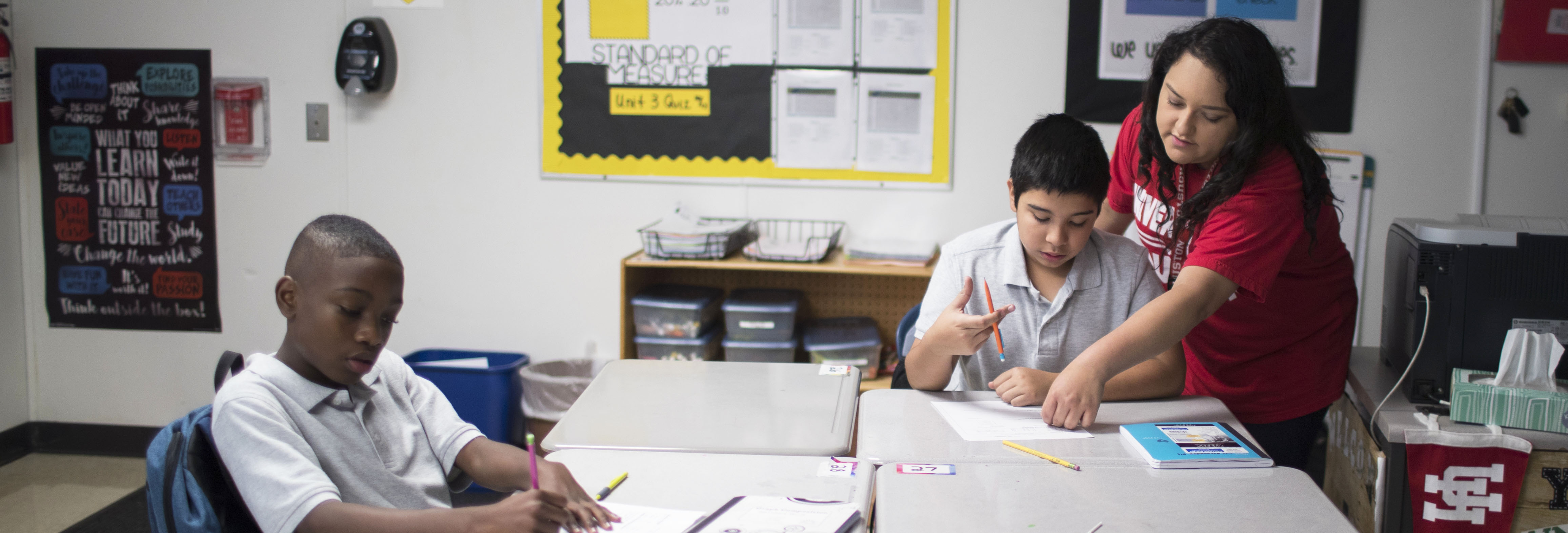 Two students working on a table with a teacher leaning over the one on the left