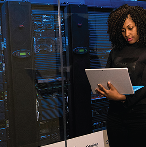 Woman using laptop while standing in front of several server racks