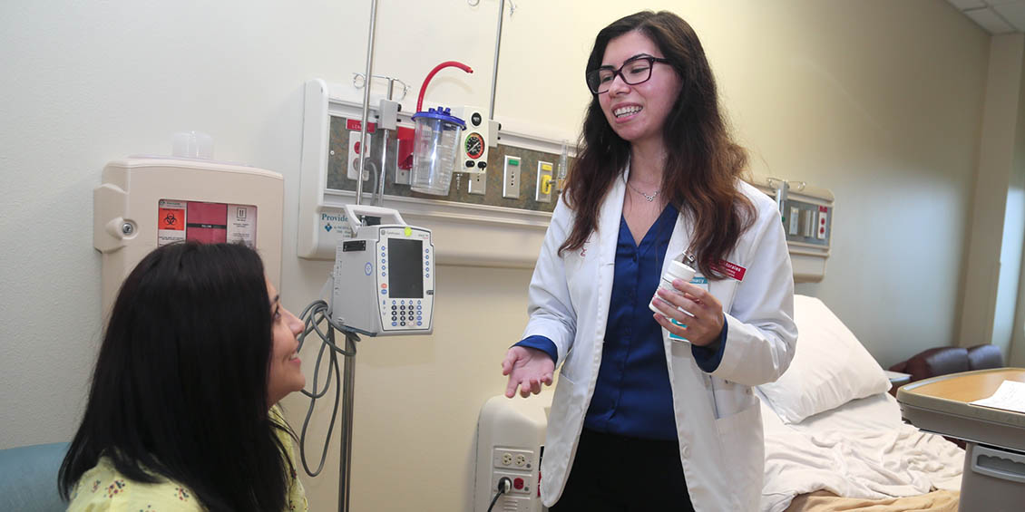 Photo of Pharm.D. student interacting with "patient" in DHR Health hospital room