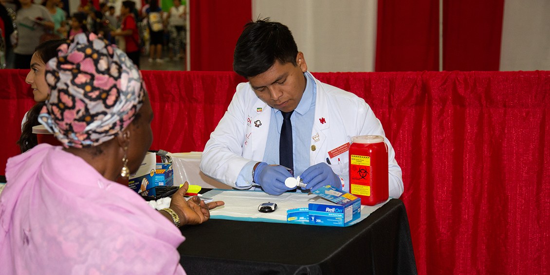 Student draws blood from patients finger.