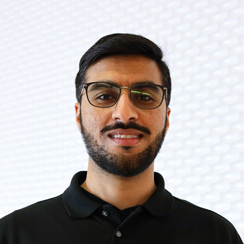 Portrait of an South Asian man smiling with a Verdi beard wearing a black polo shirt